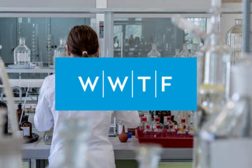 A person in a white lab coat works in a laboratory filled with glassware and bottles; a blue box with the letters WWTF covers the center of the picture.