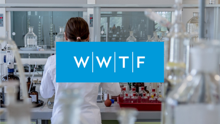 A person in a white lab coat works in a laboratory filled with glassware and bottles; a blue box with the letters WWTF covers the center of the picture.