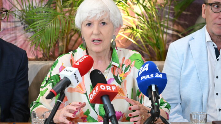 Maria Rauch-Kallat mit kurzen weißen Haaren, die eine bunte Bluse mit Blumenmuster trägt, spricht auf einer Pressekonferenz über ME/CFS in Österreich: Vier ehemalige Minister unterstützen die Petition zum PAIS-Aktionsplan. Im Hintergrund sind grüne Pflanzen zu sehen.