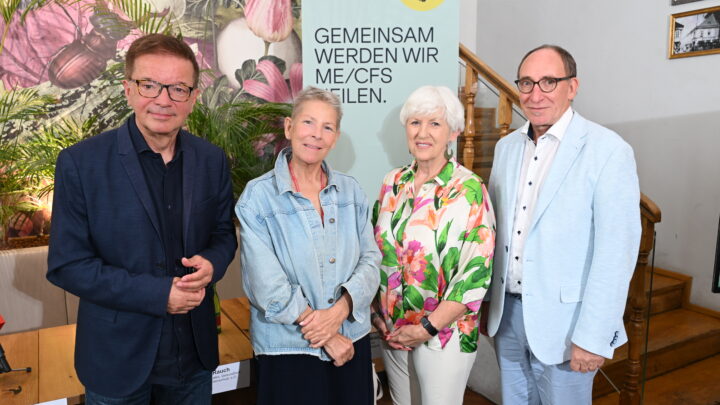 Vier ehemalige österreichische Minister stehen vor einem Transparent mit der Aufschrift „GEMEINSAM WERDEN WIR ME/CFS HEILEN“. Mit ihrem lächelnden Posieren im Ströck Feierabend in der Burggasse, machen sie darauf aufmerksam, wie ME/CFS in Österreich: Vier ehemalige Minister unterstützen die Petition zum PAIS-Aktionsplan.