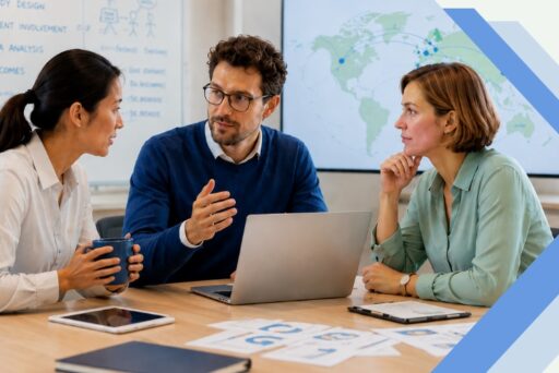 Three colleagues are sitting at a table with laptops, documents, and coffee, discussing the 2027 ME/CFS grant. Whiteboards and a world map in the background highlight the collaborative work atmosphere in their office. 